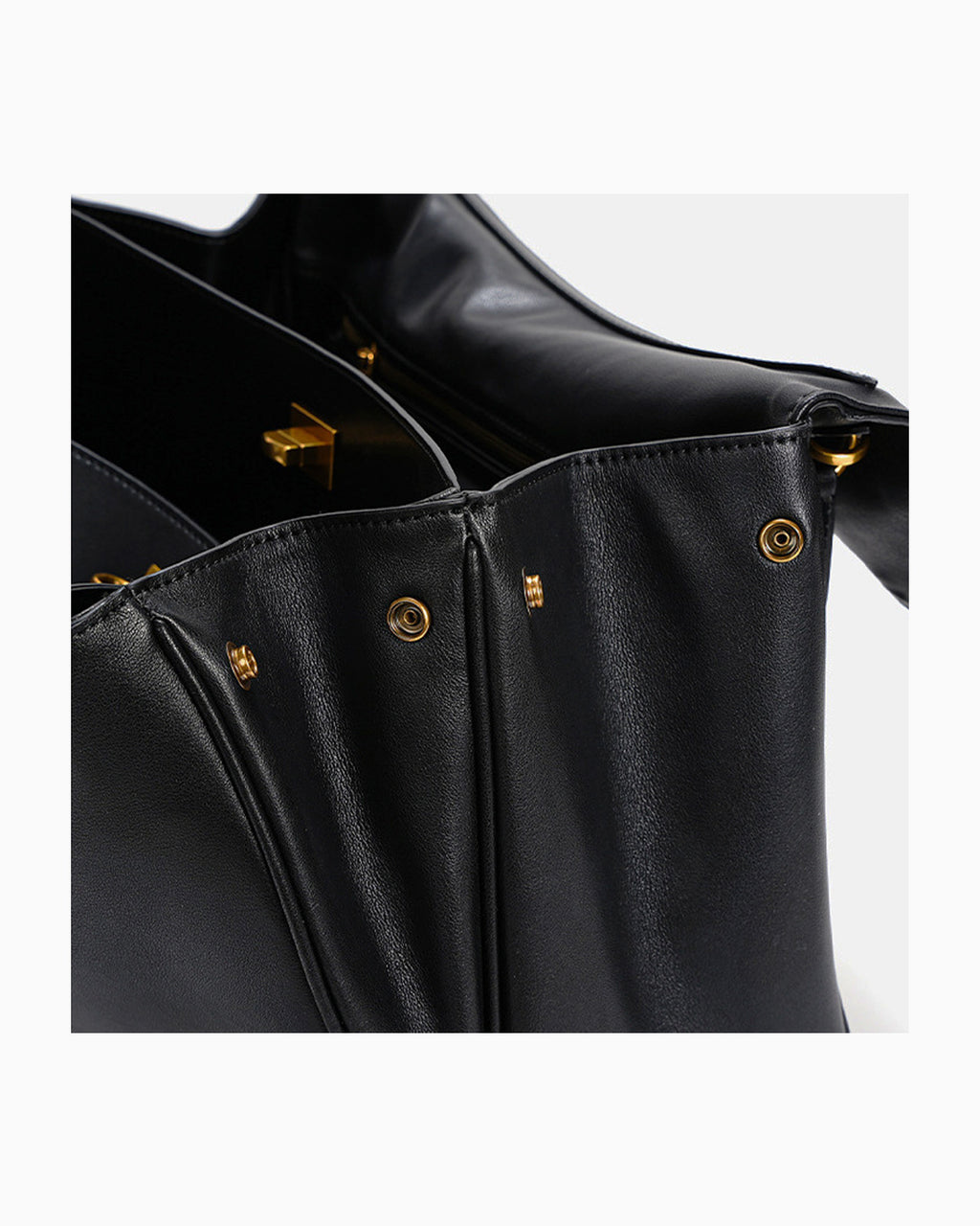 Close-up of a black leather handbag showing the interior opening, gold-tone hardware against a light gray background.