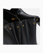 Close-up of a black leather handbag showing the interior opening, gold-tone hardware against a light gray background.