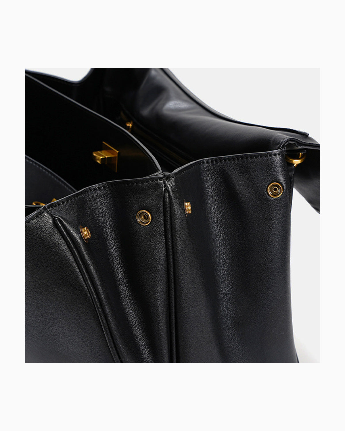 Close-up of a black leather handbag showing the interior opening, gold-tone hardware against a light gray background.