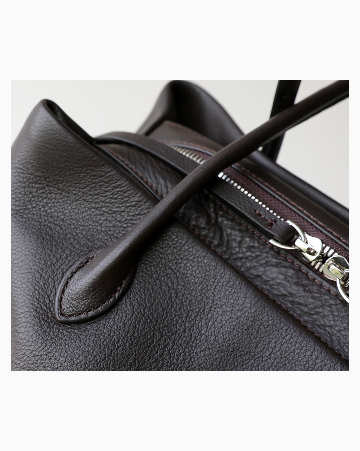 Close-up of a dark brown pebbled leather shoulder bag showing a silver zipper and a leather strap detail | BUCKLE Collective