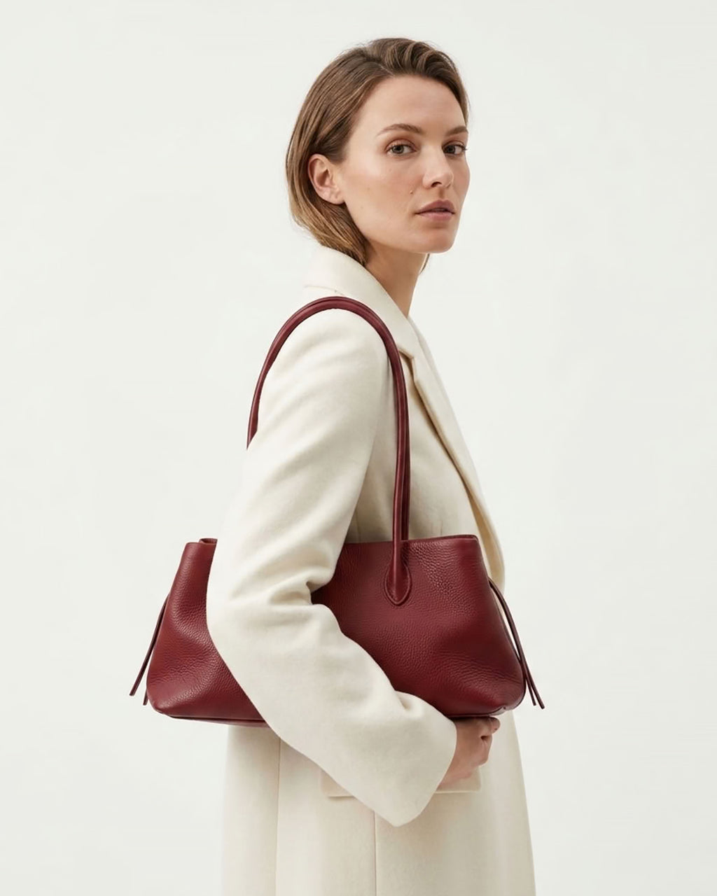 A woman in a cream-colored coat carries a large burgundy leather tote shoulder bag | BUCKLE Collective