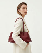 A woman in a cream-colored coat carries a large burgundy leather tote shoulder bag | BUCKLE Collective