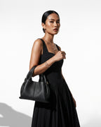 A woman in a stylish black outfit carries a Black Genuine Leather Cloud-shaped Satchel Handbag