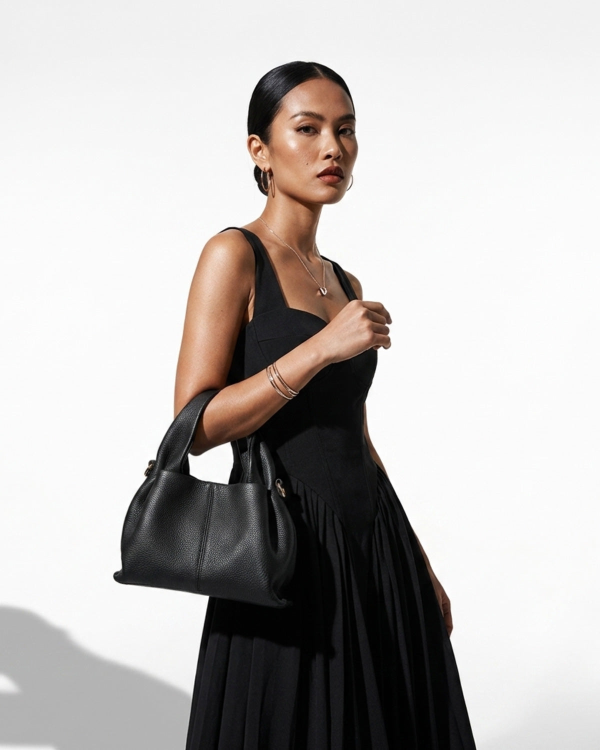 A woman in a stylish black outfit carries a Black Genuine Leather Cloud-shaped Satchel Handbag