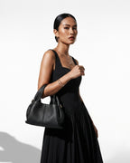 A woman in a stylish black outfit carries a Genuine Leather Black Cloud-shaped Satchel Handbag