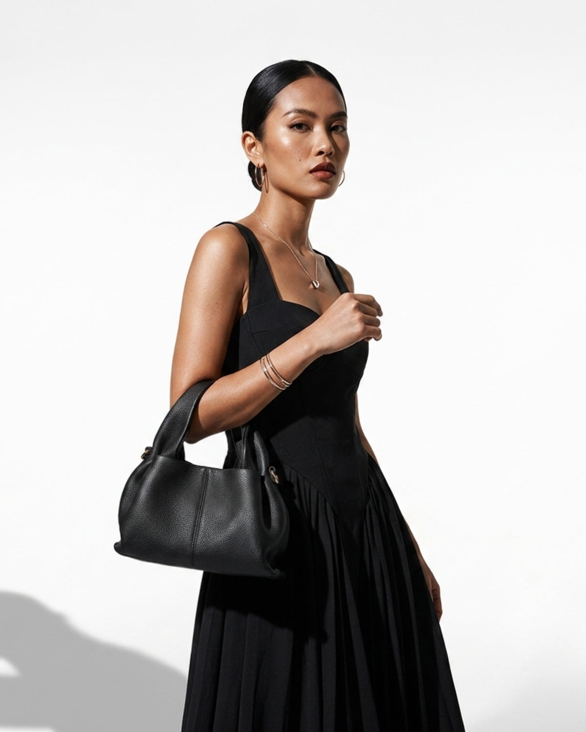A woman in a stylish black outfit carries a Genuine Leather Black Cloud-shaped Satchel Handbag