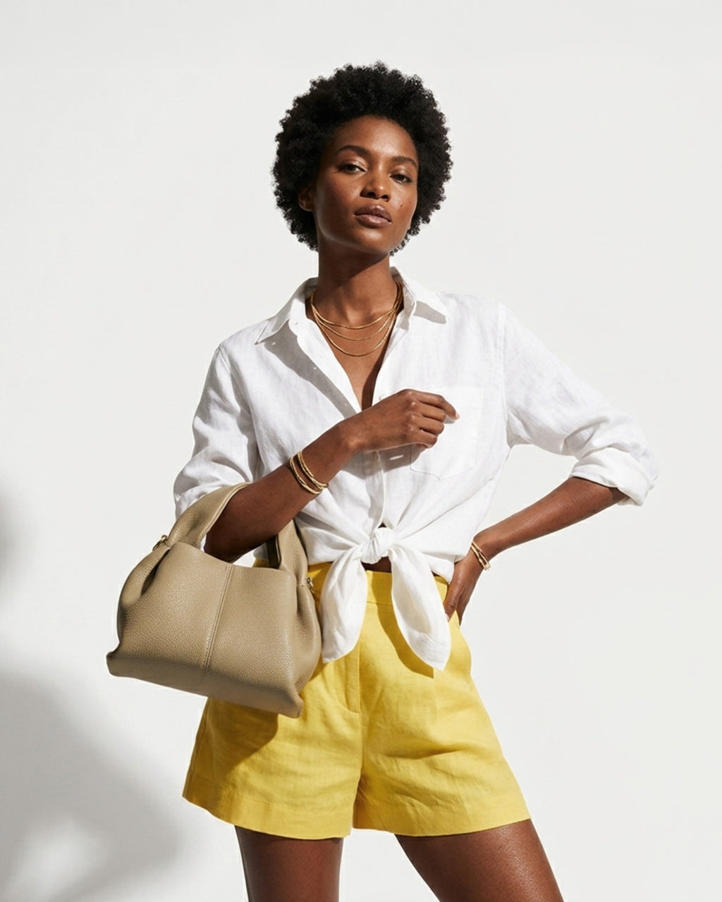 A woman in a stylish summer outfit with a white shirt and yellow shorts carries a Sand Gray Genuine Leather Cloud-shaped Satchel Handbag
