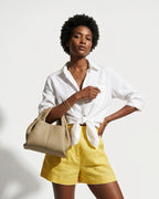 A woman in a stylish summer outfit with a white shirt and yellow shorts carries a Sand Gray Genuine Leather Cloud-shaped Satchel Handbag
