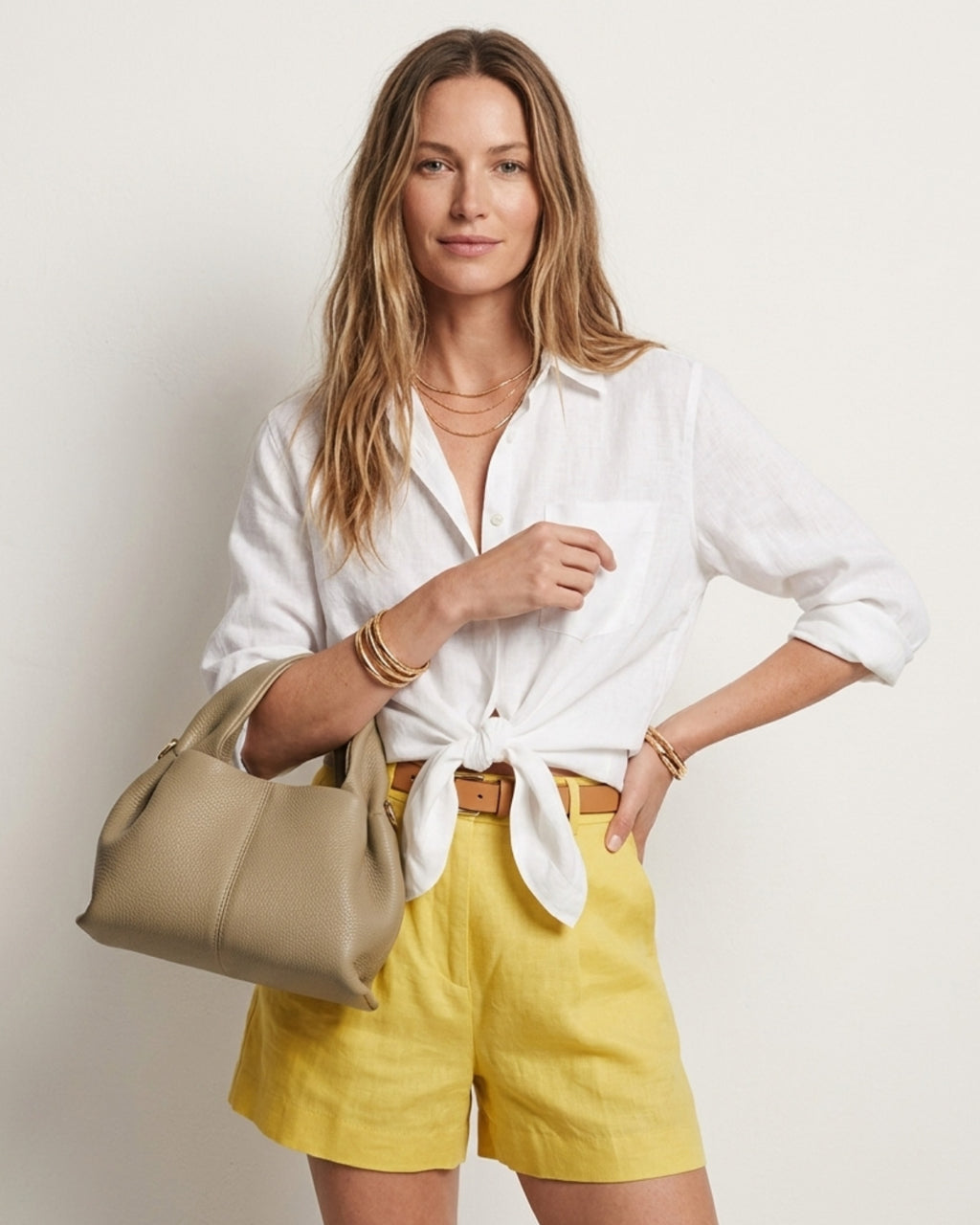 A woman in a stylish summer outfit with a white shirt and yellow shorts carries a Sand Gray Genuine Leather Cloud-shaped Satchel Handbag