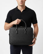 A man wearing a black polo shirt holds a black genuine ostrich leather briefcase by BUCKLE Collective