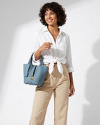 An elegant woman in a stylish casual outfit holds a Genuine Togo Leather Bucket Bag in Misty Blue color with a lock and Key