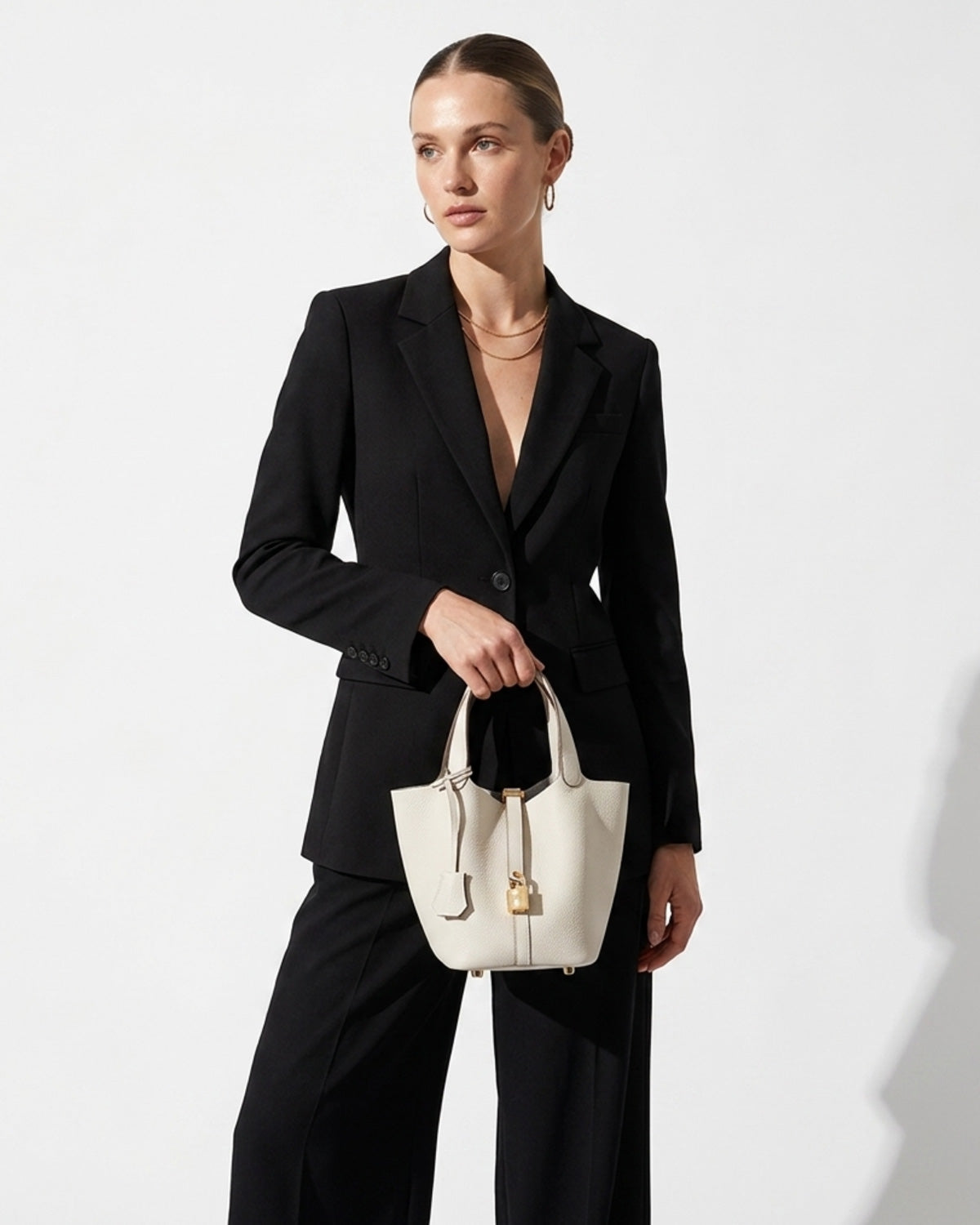 Fashionable woman in black stylish outfit holds a Genuine Togo Leather Bucket Bag with Lock and Key, Off-White color