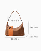 A light brown woven shoulder bag shown on a light gray background with overlaid dimension lines and measurements for width, height, and strap length, plus a phone placed iin fornt of the bag for scale.
