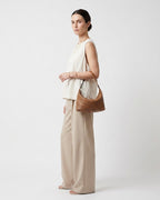 A woman stands in profile wearing a sleeveless cream top and beige wide-leg pants, carrying a light brown genuine woven leather shoulder bag | BUCKLE Collective