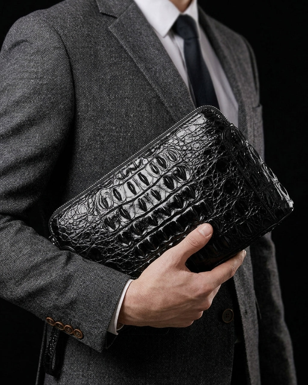A man in a gray suit and tie holding a Black Genuine Siamese Crocodile Leather Clutch with a top zipper and a matching wrist strap