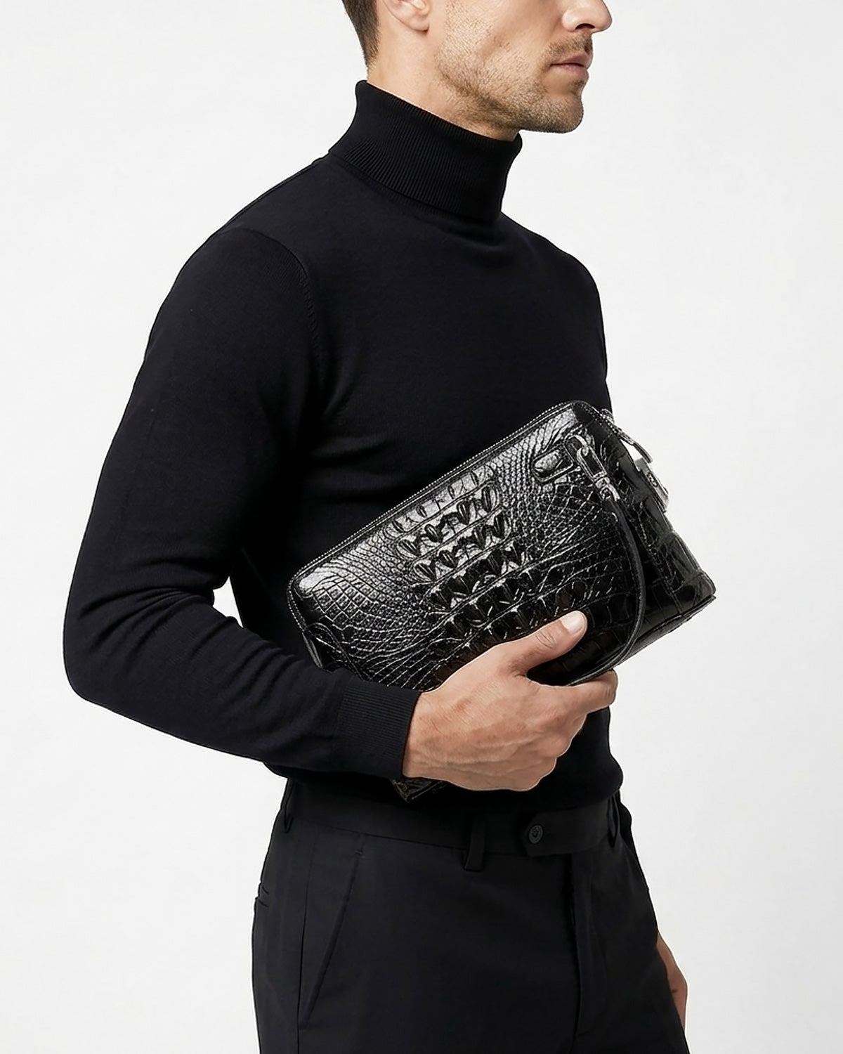 A man in a black turtleneck sweater and black trousers holds a black Genuine Crocodile Leather Clutch with a combination lock by BUCKLE Collective