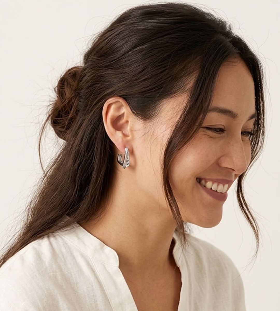 Model wearing a silver-tone geometric hoop earring with ribbed detailing, styled with a white blouse and half-up hair.