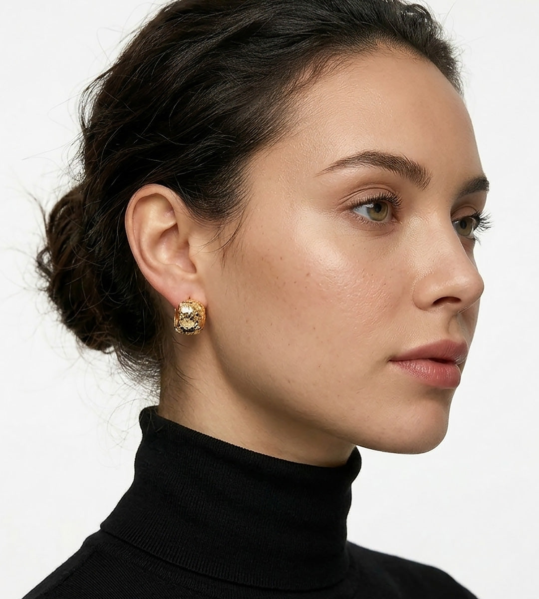 A close-up side profile of a woman with dark hair in a bun, wearing Glitter Textured Pillow Huggie Earrings | 18K Gold Plated S925 Silver | BUCKLE Collective