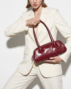 Elegant Woman in a white fashionable outfit wearing a genuine leather baguette shoulder bag in burgundy color