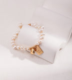 Good Luck baroque pearl bracelet worn on wrist in vintage gold — "Good Luck" tag and heart charm detail, styled with gold rings and pearl necklace, 18K gold plated S925 silver, BUCKLE Collective

