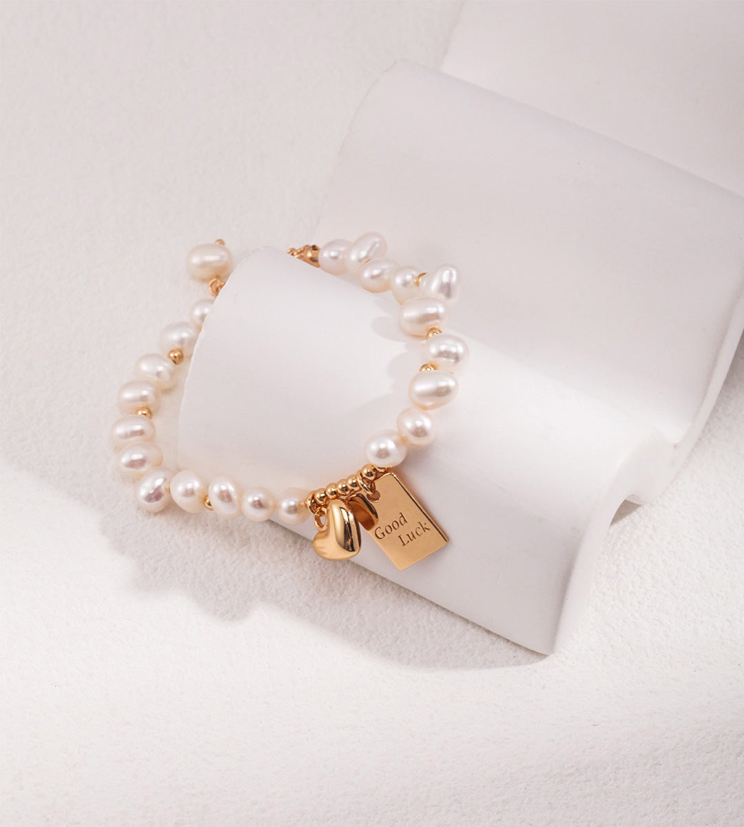 Good Luck baroque pearl bracelet worn on wrist in vintage gold — "Good Luck" tag and heart charm detail, styled with gold rings and pearl necklace, 18K gold plated S925 silver, BUCKLE Collective

