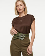 A woman wearing a brown short-sleeved top and olive-green trousers, accessorized with a wide green double-buckle statement belt | BUCKLE Collective