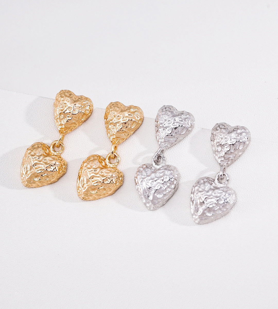 Four textured heart-shaped drop earrings arranged in two pairs of one gold-tone and one silver-tone, on a clean white background.