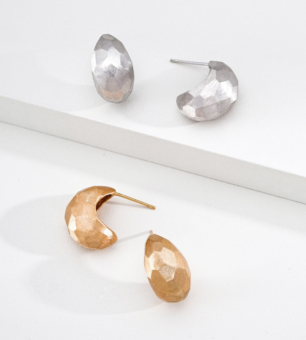 A pair of 18K gold-plated faceted crescent-shaped drop earrings and a pair of 18K white-gold-plated faceted crescent-shaped drop earrings are displayed on a clean white surface.