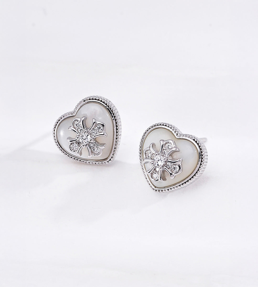 Silver tone heart shaped mother-of-pearl stud earrings with cubic zirconia-set flower centres and finely beaded metal borders.