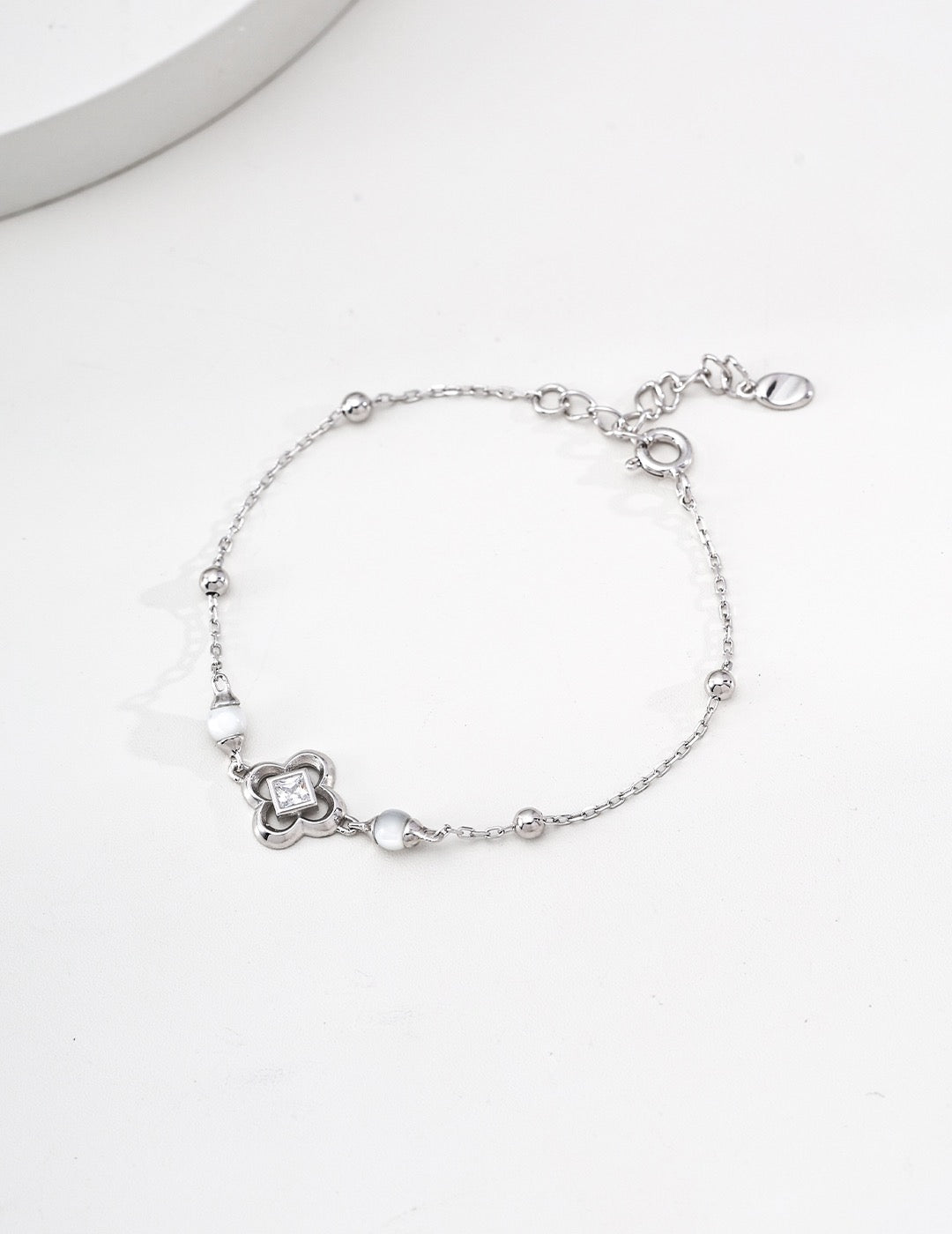 Silver-tone clover bracelet with square cubic zirconia, white shell beads and polished ball accents, showing the spring-ring clasp and extender.