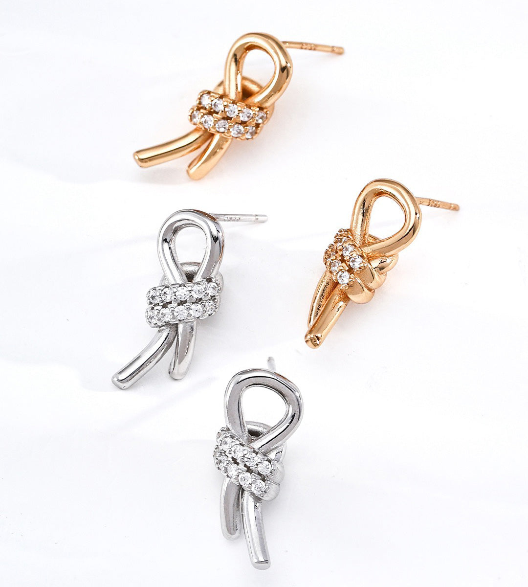 Two pairs of bow-shaped stud earrings on a white background, including two gold-tone and one silver-tone pair, each with a row of clear stones at the center.