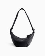 A black crescent-shaped shoulder bag with a single strap, featuring a quilted texture and a zippered top closure by BUCKLE Collective