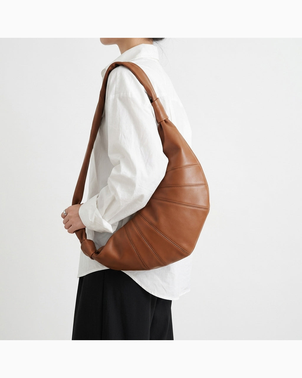 A person wearing a white button-up shirt and black skirt carries a large light brown lambskin leather crescent-shaped hobo shoulder bag | BUCKLE Collective