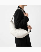A woman wearing a black outfit carries a large, soft, slouchy crescent-shaped shoulder bag in off-white genuine lambskin leather | BUCKLE Collective