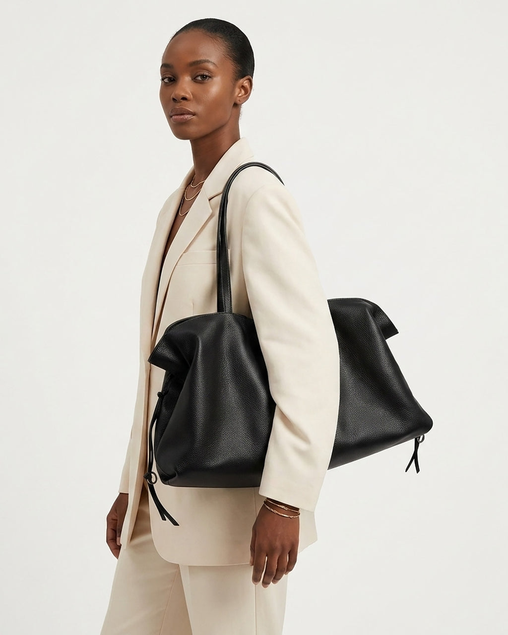 A model in a cream-colored blazer and trousers carries a large black leather tote bag over her shoulder