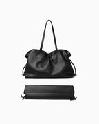 A black leather slouchy tote bag with a long strap, shown from the back and bottom sides