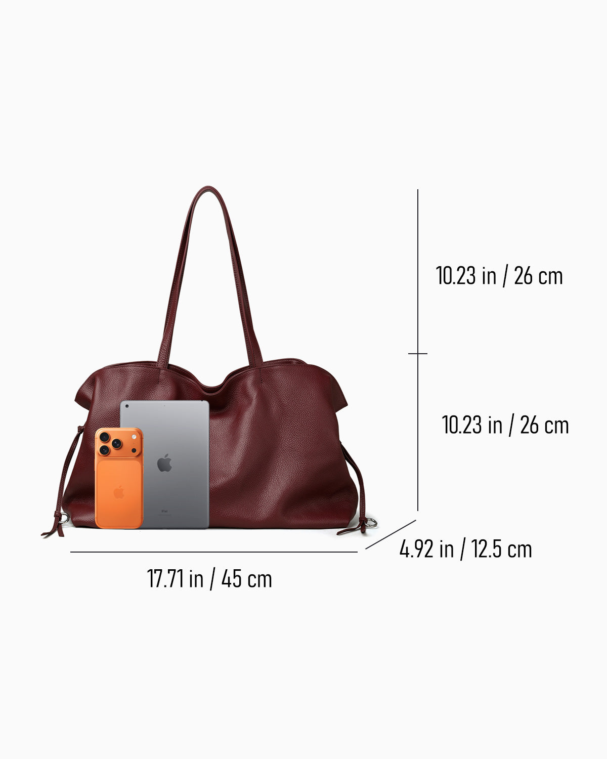 A burgundy leather tote bag shown with dimension lines and measurements on a light gray background, alongside a smartphone and tablet for scale.