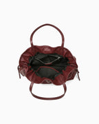 A top-down view of a burgundy leather slouchy tote bag with its open interior showing a black lining, zip pocket, and slip pocket