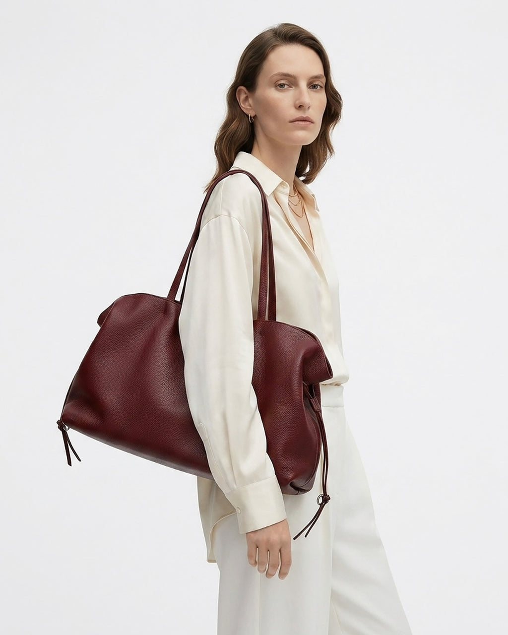 A woman in a white shirt and trousers carries a large burgundy leather tote bag over her shoulder. BUCKLE Collective