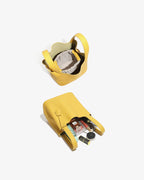 A yellow bucket bag shown from above in two views on a light grey background: one closed and one open, revealing an interior with a light grey inner pouch and contents including cosmetics.