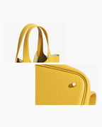A close-up product image of a bright yellow Togo leather bucket bag, showing the top handles and bottom detail