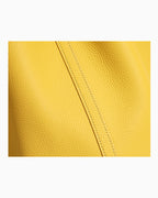 A close-up of a bright yellow pebbled leather surface with a diagonal stitched seam running through the center