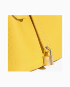 Close-up of a bright yellow pebbled leather bucket handbag with a gold padlock and strap detail