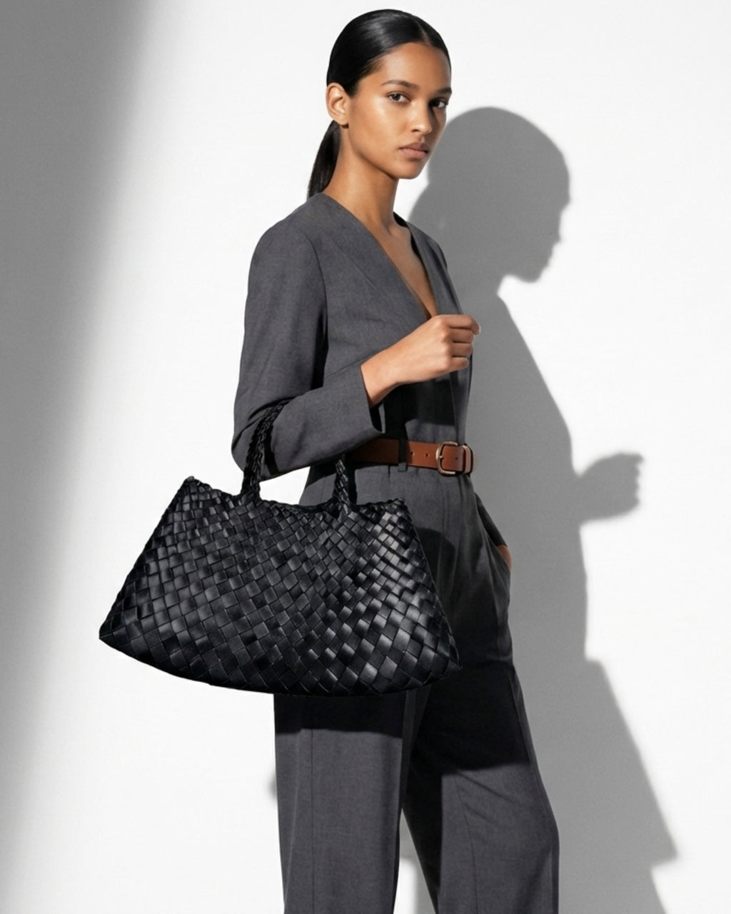 A woman in a stylish gray outfit carries a Trendy & Spacious Genuine Leather Woven Handbag with Removable Pouch in Black Color