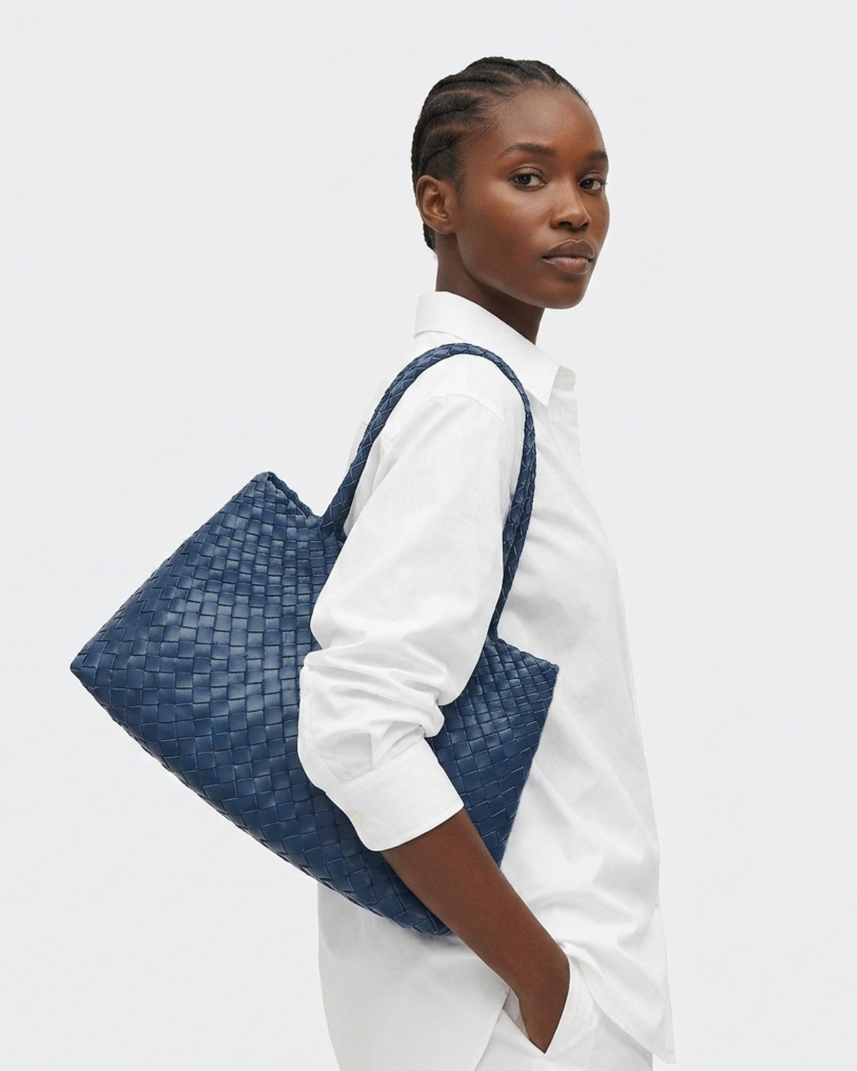 A woman in a white shirt carries a large woven blue tote bag over her shoulder