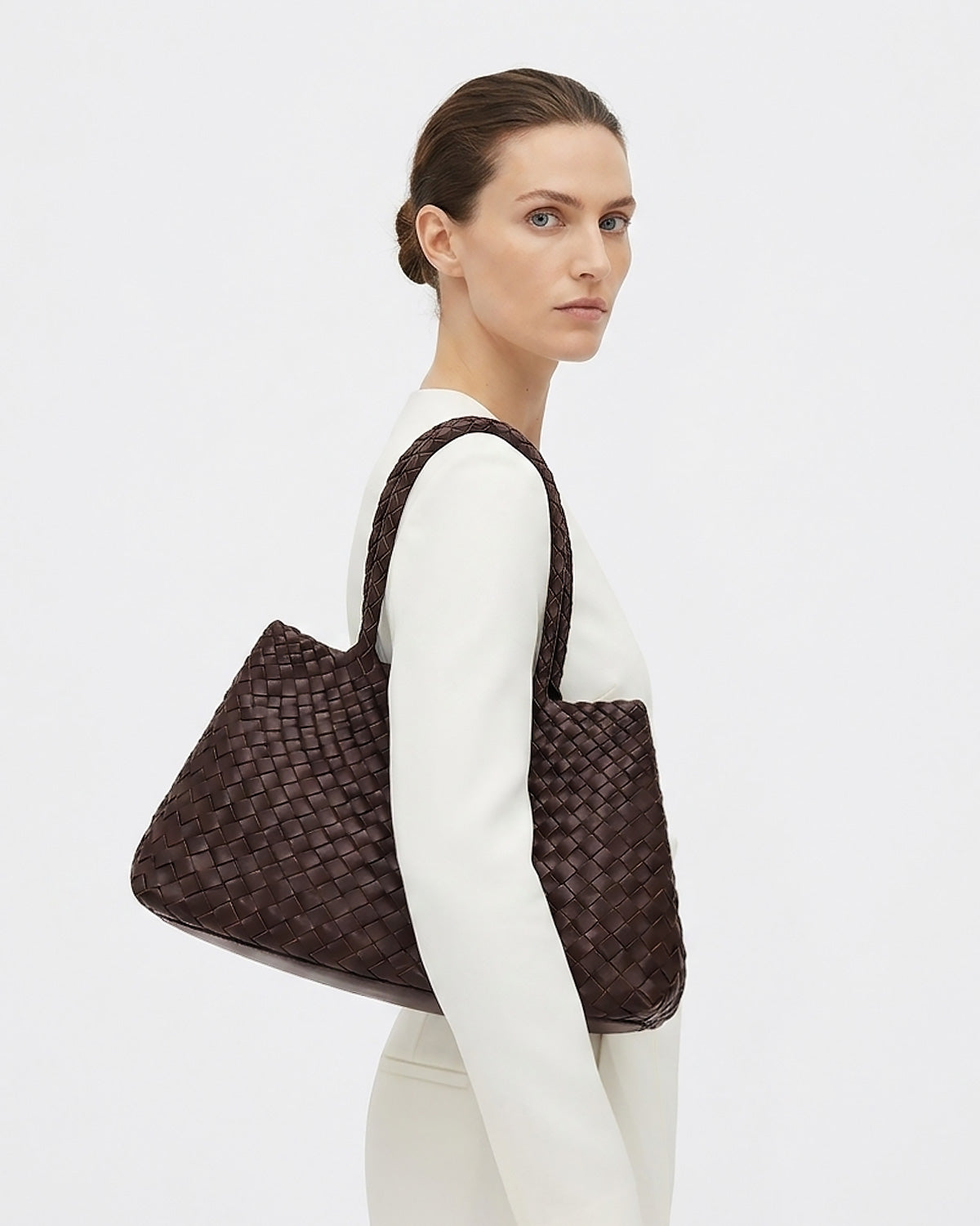 A woman in a white sweater and white pants carries a large Woven Genuine Leather Tote Bag over her shoulder