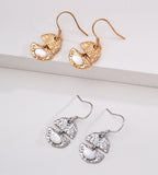 Two pairs of dangling earrings are displayed on a white surface: one pair in 18K gold-plated S925 Silver and one pair in 18K white-gold-plated S925 Silver | BUCKLE Collective