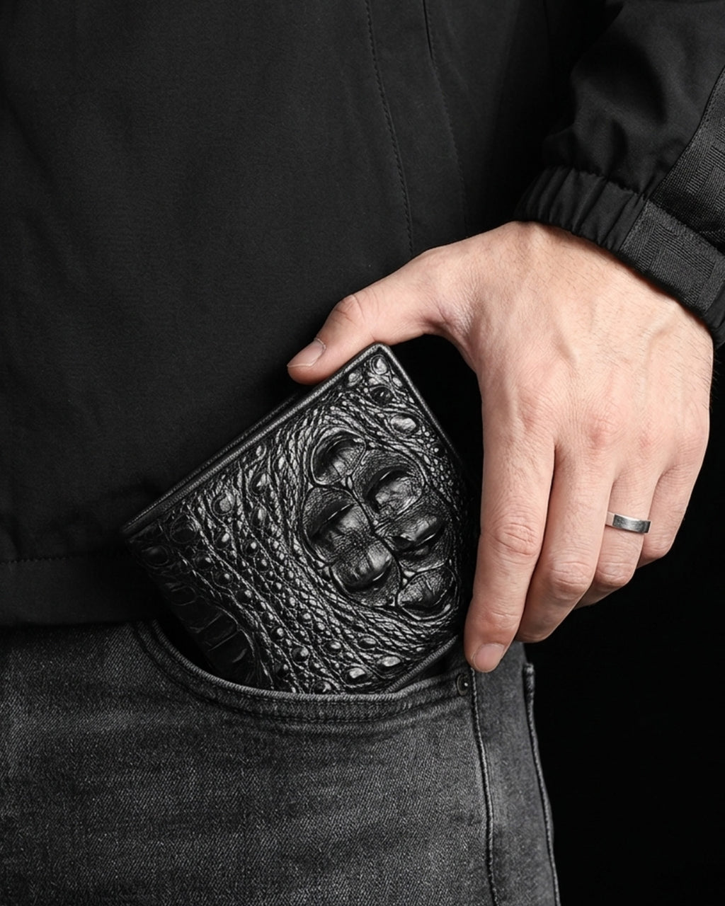 A close-up of a person's hand holding a black Genuine Crocodile Leather Wallet in their pocket, wearing a black jacket and dark gray jeans.