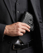 A close-up of a man in a black suit holding a Black Genuine Crocodile Leather Wallet