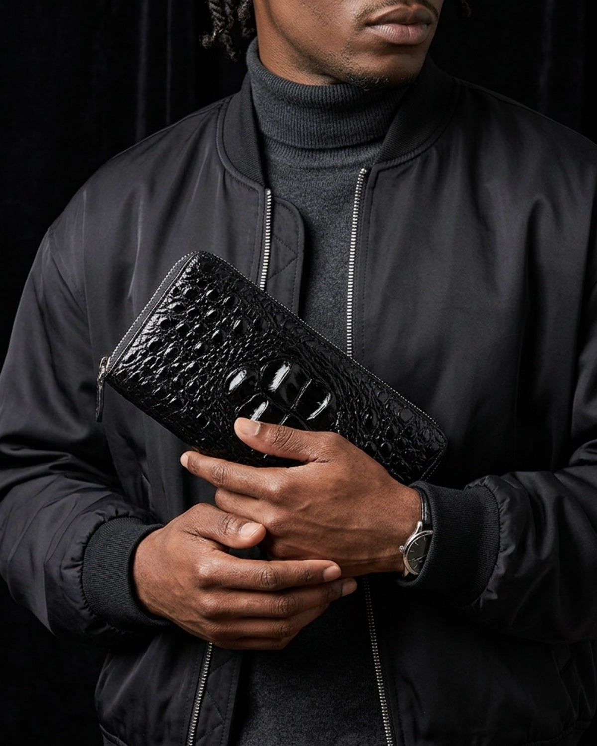 A man wearing a black bomber jacket and gray turtleneck holds a Genuine Siamese Crocodile Leather Clutch